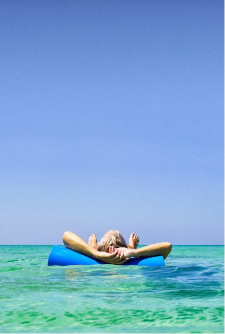 Person lying on a blue float in clear turquoise sea under a clear blue sky.